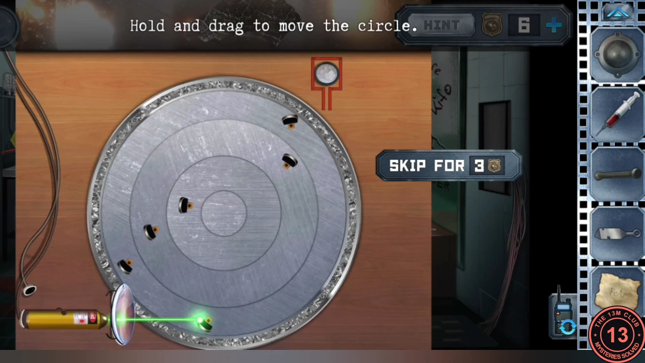 The laser pointer behind the lens shining a green beam onto a round metal plate with concentric rings and several small mirrors, with the target button at the top right; instruction 'Hold and drag to move the circle'