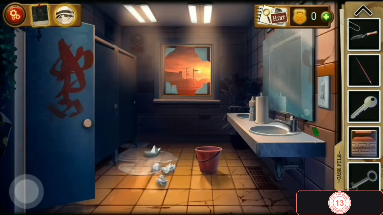 Restroom with an open blue stall door covered in red graffiti on the left, crumpled paper on the floor, a red bucket in the middle and sinks with a mirror on the right