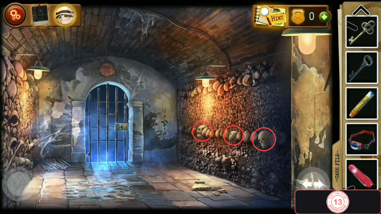 Catacomb corridor with a blue barred gate at the end and walls of stacked skulls; three white skulls sticking out of the middle row on the right wall are circled