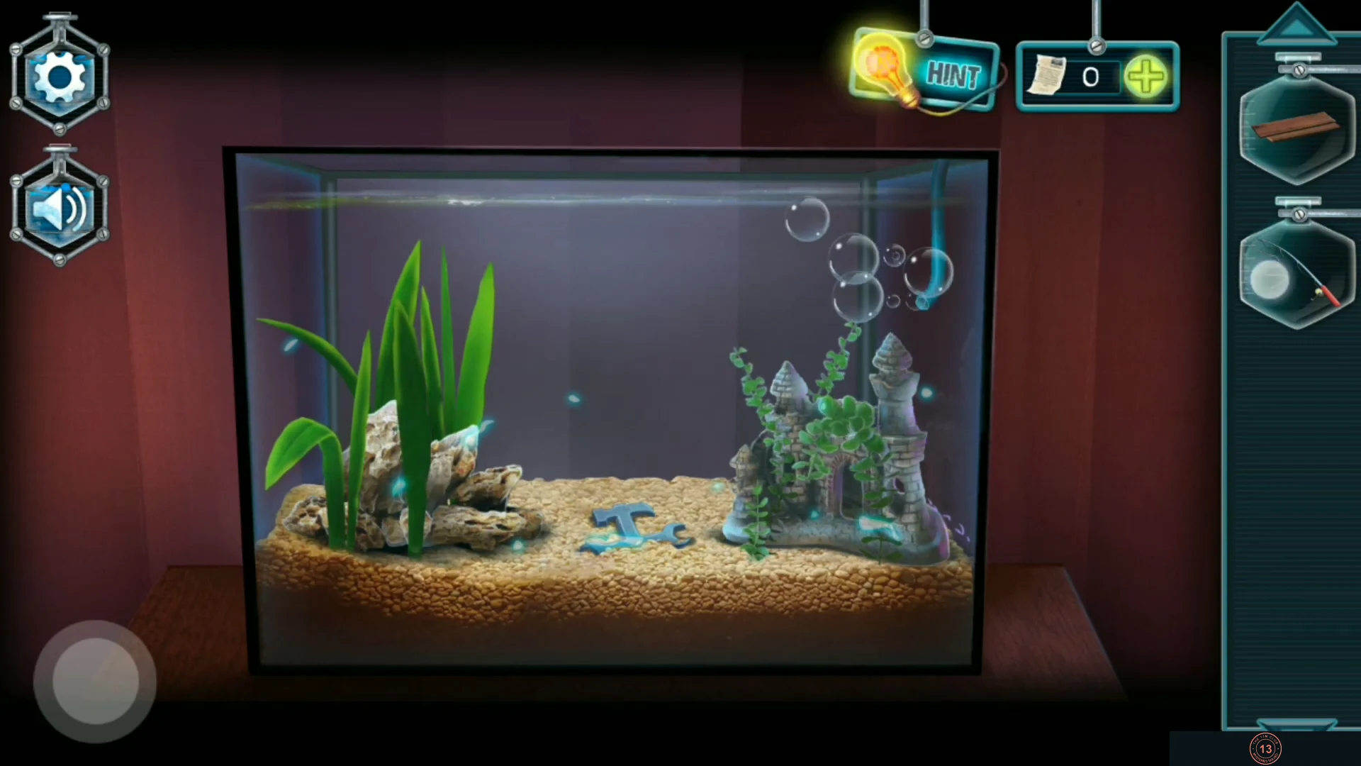 Lit aquarium with plants, a castle ornament and the cross-shaped hammer-and-wrench piece lying on the gravel