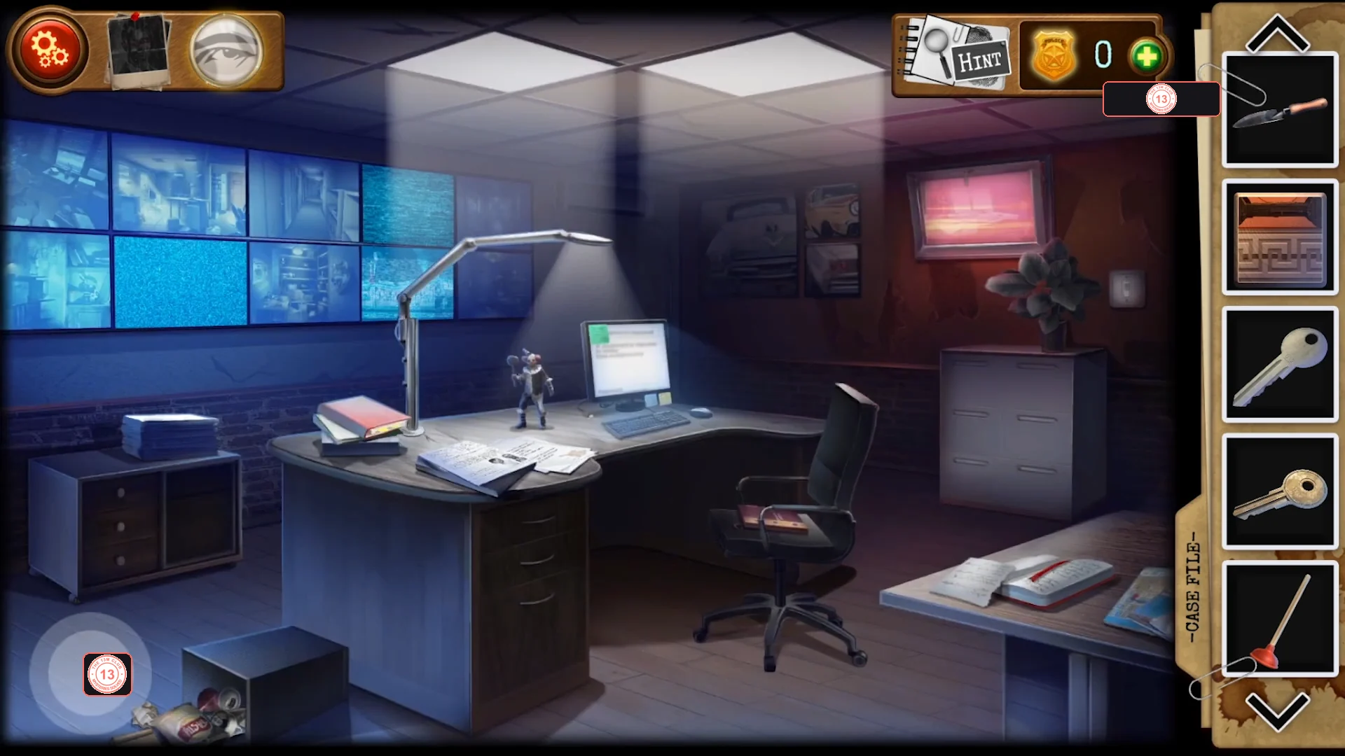 Security room with a wall of monitors, a desk with a computer, books, a note and a clown statuette, a cardboard box on the floor and a filing cabinet with a plant on the right