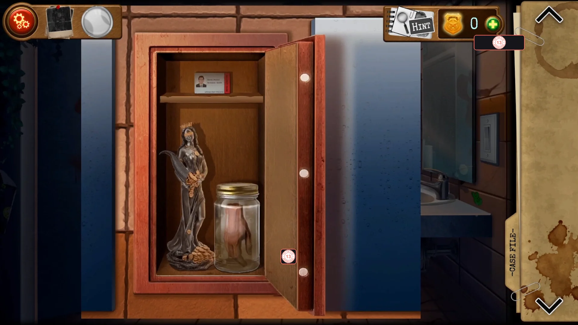 Open wall safe behind the mirror holding a dark statuette, a glass jar with a severed hand and a security pass on the top shelf